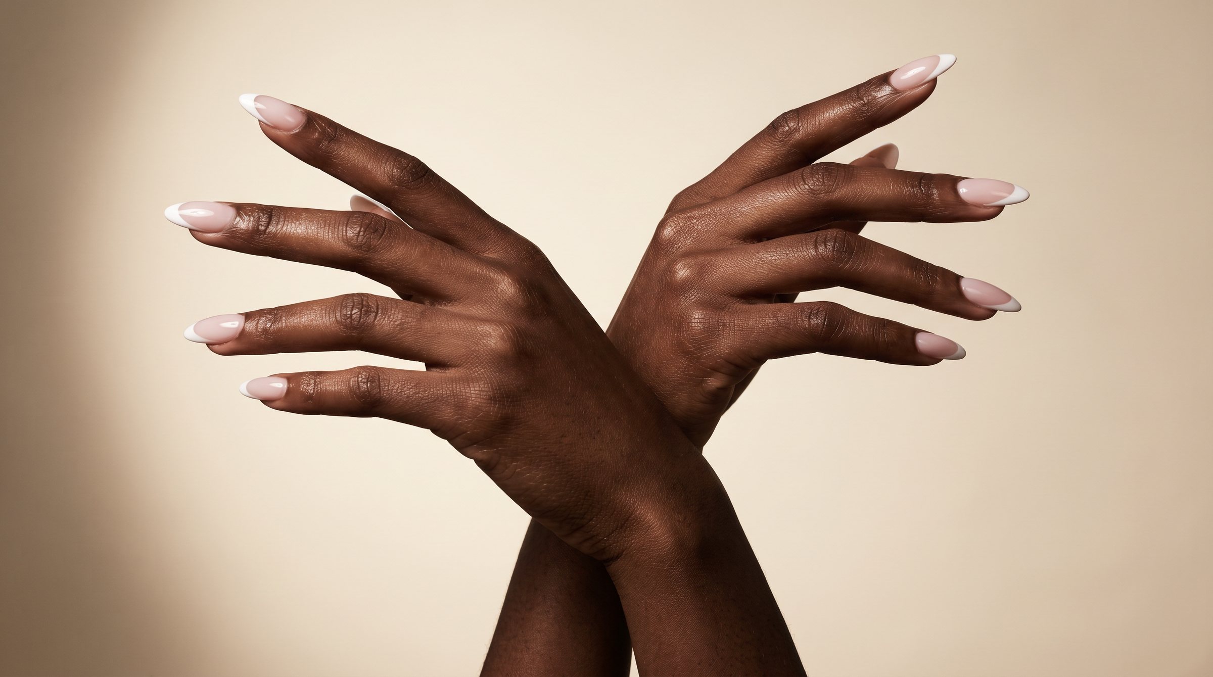 A pair of hands with long almond nails and crisp white French tips, crossed in an editorial pose